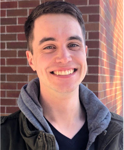 A portrait of Carson with a red brick wall in the background. He is smiling, because he has not yet experienced the horrors of grad school.